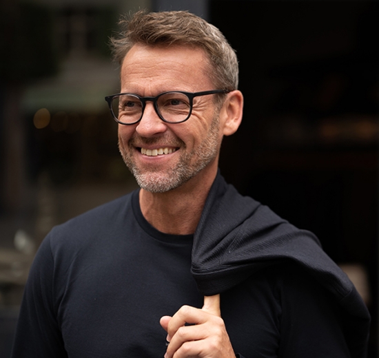 Mann mit Brille, hängt Jacke über die Schulter. 