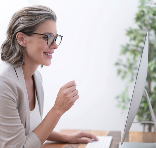 Frau mit Brille sitzt am Schreibtisch und schaut in Ihren Bildschirm.