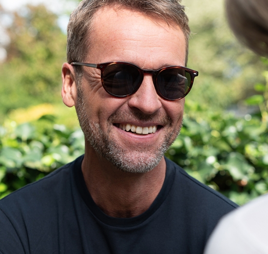 Mann mit Sonnenbrille steht im Grünen. 